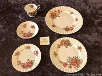 Full place setting including one dinner plate, one salad plate, one bread and butter plate, one teacup and one saucer with floral rose pattern on dark background