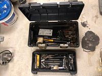Top view of open black Stanley toolbox, showing assorted hand tools inside including a yellow-handled hammer and pliers.