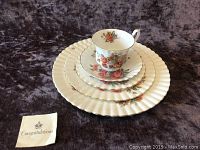 Full view of all five pieces stacked: dinner plate, salad plate, bread & butter plate, saucer, and teacup on top showing floral rose pattern and fluted edges.