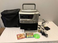 Full view of Venturer karaoke machine, two karaoke CDs, and soft carrying case on a table.
