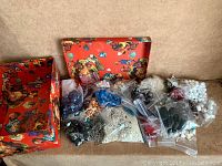 Red decorative box with lid open showing multiple small resealable plastic bags filled with assorted beads in various colors and sizes.