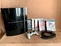 Photo showing Sony PlayStation 3 console with silver wired controller and five PS3 game cases including Madden NFL 25, NBA 2K11, FIFA Soccer 13, and two other titles, along with cables.