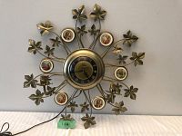 Front view of vintage decorative wall clock showing central clock face, floral metal leaves, and portrait inserts