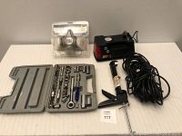 Photo showing socket wrench set with various sockets and extensions, black car air compressor, caulking gun or sealant applicator, and long black power cord
