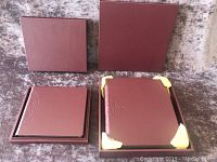 Two burgundy leather look embossed photo albums in their open boxes and a matching case, showing the albums' covers and corners.