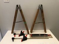Whole lot including two wooden saw horses, four spring clamps, and a packaged laser level on a white surface