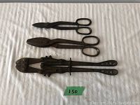 Three vintage hand tools laid on fabric: long handled bolt cutters, two pairs of tin snips (medium and large size).