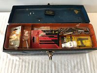 Open blue metal toolbox showing drill bits, accessories, and a light bulb inside the top compartment and tray.