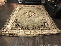 Full view of the large area rug laid flat on a wood floor, showing the entire design and curled edges.