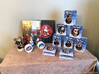 Photo of entire lot including gift boxes with Santa Claus artwork, stacked boxed Christmas ornaments, and Christmas figurines and candles arranged on a table.