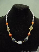 Full view of beaded women's necklace with a variety of stone cabochons and beads on a black bust stand.