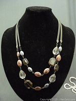 Full view of vintage costume jewelry necklace on black display showing two strands with faceted amber and clear beads along with matte pink and silver beads strung on white cords.