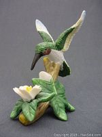 Full view of the vintage ceramic hummingbird figurine perched above ceramic flowers and leaves on a black background.