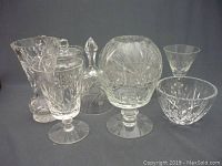 Seven assorted vintage crystal and glassware items including goblets, bell, sugar bowl with lid, and snifter glass.