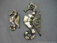 Two resin and shell seahorse wall plaques on a black background, showing size difference and overall condition.