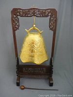 Full view of the brass gong suspended on an ornately carved wooden stand with mallet beside it.