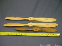 Three wooden model airplane propellers laid horizontally with measuring tape showing lengths ranging from about 8 to 12 inches.