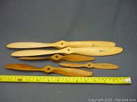 Five wooden model airplane propellers laid side by side with measuring tape for scale.