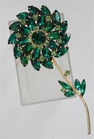 Full front view showing the entire flower brooch with green marquis rhinestones and smaller light green rhinestones on a golden stem.