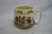 Front angle of the Royal Doulton Bunnykins porcelain mug showing bunnies reading a newspaper with a bunny border near the rim.