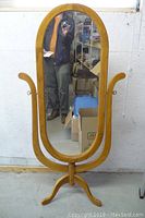 Front view of the vintage oak-framed standing mirror, showing oval glass and wooden frame with curved legs.