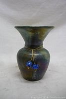 Front view of small glazed pottery vase with attached blue dice charm on gold chain.