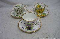 Photo showing three fine bone porcelain teacups and saucers, each with different floral patterns and gold trim.