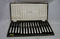 Full view of set in open black leather-like canteen case lined with cream satin interior and black insert holding 6 forks and 6 knives.