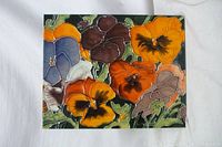 Top-down view of the ceramic tile showing a colorful glazed poppy flower design with multiple flowers in orange, yellow, brown, blue, and purple shades.
