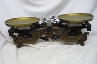 Full view of the antique weighing scale showing two round brass pans and cast iron base with decorative elements.