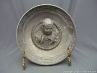 Full front view of pewter bowl on stand showing central child bust and ornate rim pattern