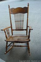 Front view of antique wooden rocking chair showing pressback with spindle supports and armrests.