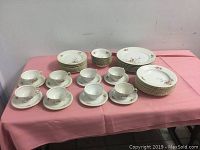 Full set displayed on pink cloth showing arrangement of plates, bowls, cups and saucers.
