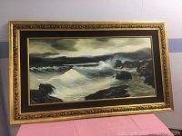 Full view of the framed original oil on canvas seascape painting showing crashing waves and rocky shore, mounted in an ornate gold-painted frame.
