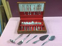 Full set of silverware in a wooden box with red velvet interior showing the entire collection of spoons, forks, knives, and serving pieces.
