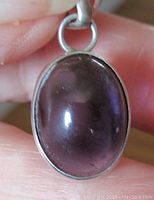 Front view of the oval amethyst cabochon in silver bezel setting, showing deep purple color and polished finish.