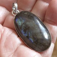 Close-up of front side of oval labradorite pendant showing stone and silver tone metal setting held in hand.
