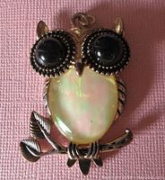 Front view of the gold tone owl pendant showing the mother of pearl body and black stone eyes on a branch.