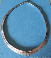 Full view of two tone sterling silver modernist necklace on blue background, showing overall shape and design.