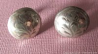 Front view of the vintage round sterling silver earrings showing floral engraving on a textured pink background.