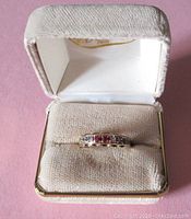 Ring in cream-colored padded jewelry box showing front and setting.