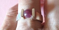 Front view of sterling silver ring worn on finger showing round dark pink cabochon stone.