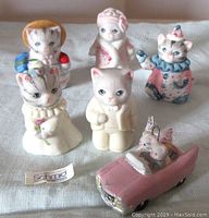 Front view showing six porcelain cat figurines and one bridal car figurine with a Schmid label on cloth surface.