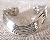 Front view of a heavy sterling silver bangle bracelet with curvy multi-stripe design on a neutral fabric background.