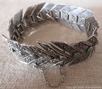 Sterling silver link bracelet laid out showing V-shaped links, floral and leafy design elements, green bezel-set stones, and attached safety chain.