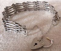 Top view of silver bracelet showcasing the gate style five-bar links and heart-shaped padlock clasp attached with safety chain.
