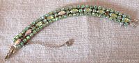 Full bracelet laid flat showing two rows of green Aurora Borealis glass stones and safety chain, silver tone metal.