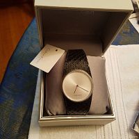 Calvin Klein Swiss made watch inside original branded gray box with attached tag and leather strap on gray pillow