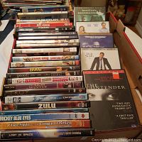 Photo of the lot of DVDs showing full height and width of DVDs in a box, titles on the spines and front covers are mostly visible.