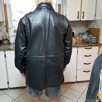 Rear view of the black leather jacket displayed on a person, showing the smooth back and long length.